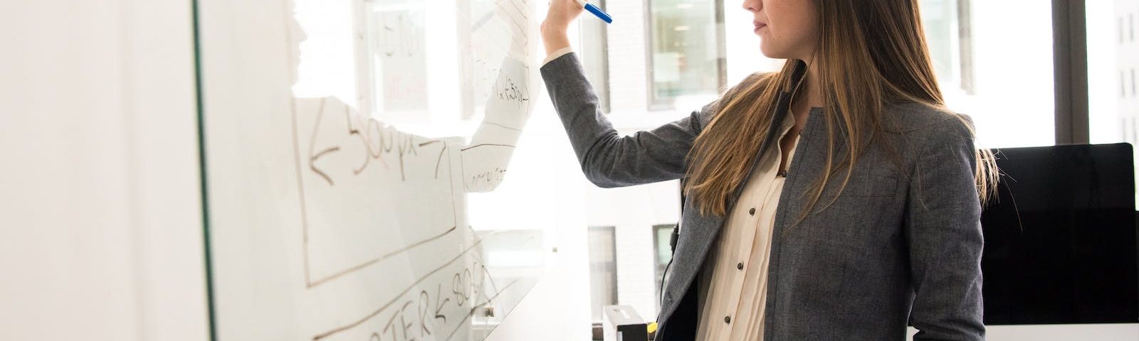 Woman Wearing Gray Blazer Writing on Dry-erase Board